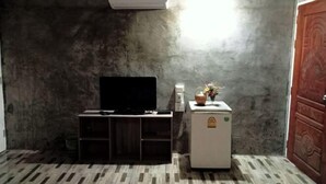 A room with a flat-screen TV on a wooden stand, a small refrigerator, and a wall-mounted air conditioner. - Ingna Resort (Chanuman)