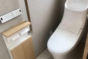 Une salle de bain moderne équipée de toilettes, d’un meuble en bois et d’une prise électrique murale.