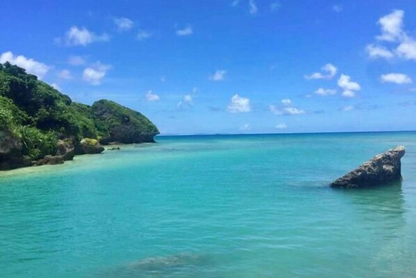 Un paysage côtier caractérisé par une eau turquoise cristalline, un promontoire rocheux et une végétation luxuriante.