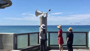 Um píer com grade de metal, um pilar de concreto com um megafone e uma vista ampla do oceano.