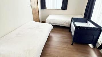 Quarto com duas camas, um berço, piso de madeira e uma janela com cortinas.