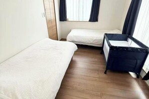 A room with two beds, a crib, wooden flooring, and a window with curtains. - ZZOKIAI Blue Fish! Only 2 mins to beach by walk! Maximun 11 persons! (Itoman)