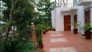 A courtyard with potted plants, a tiled walkway, and a white building with a wooden door. - Nicole's Garden Naga (Naga)