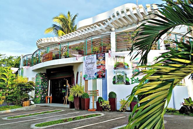 A building with a curved entrance, potted plants, and a signboard.