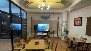 A dining area with wooden tables and chairs, a television screen, and a decorative plant. - Nicole's Garden Naga (Naga)