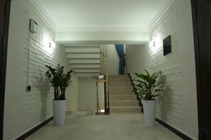 Un pasillo con una escalera, plantas en macetas y una lámpara.