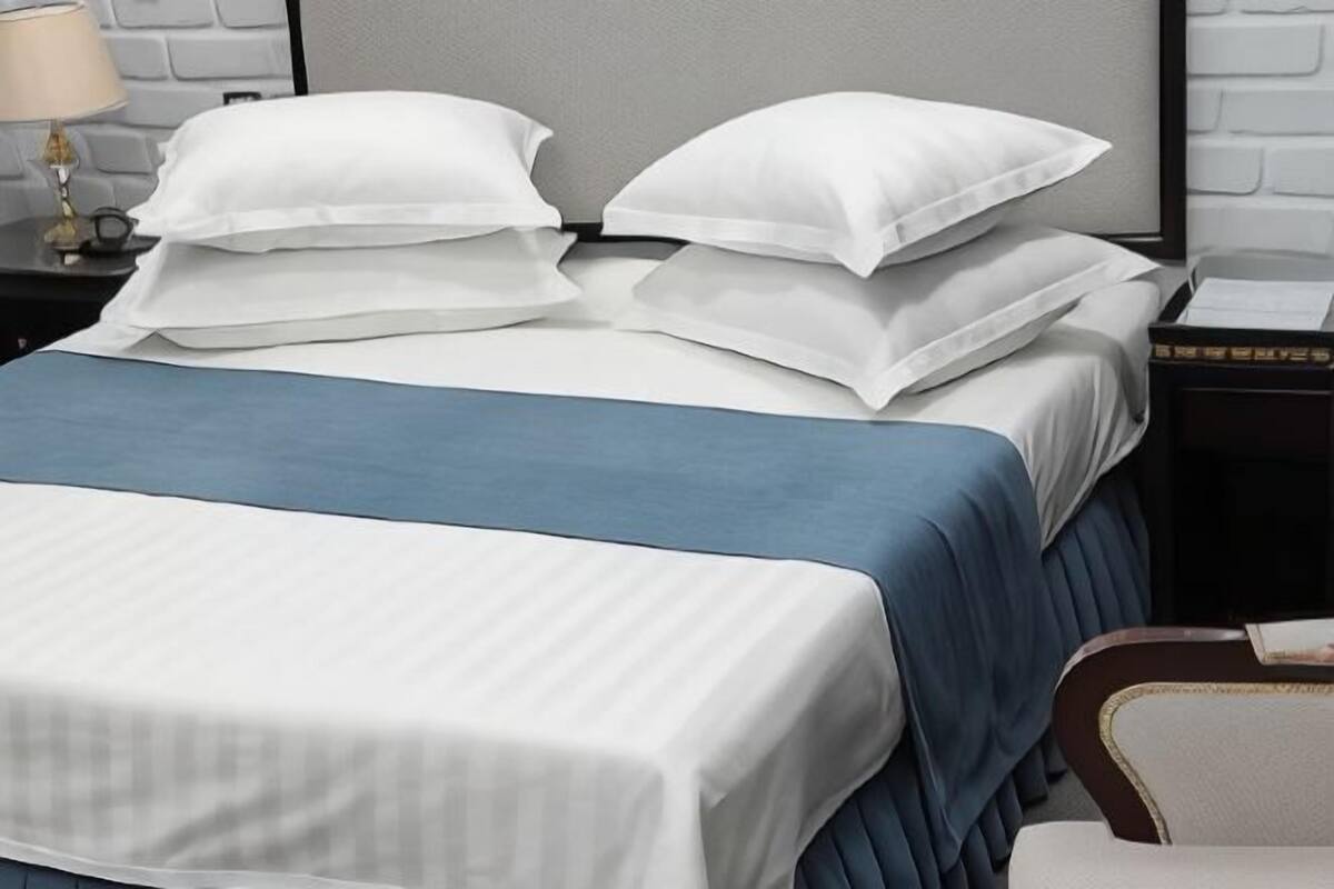 Een bed met witte beddengoed en blauwe accenten, een nachtkastje met een lamp, en een lijst met een afbeelding aan de muur.
