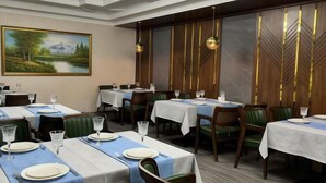 A dining area with tables set for service, a large landscape painting on the wall, and a decorative wall panel with vertical lines. - ZA'Faron Hotel Jizzax-Department of Management Only (Jizzakh District)