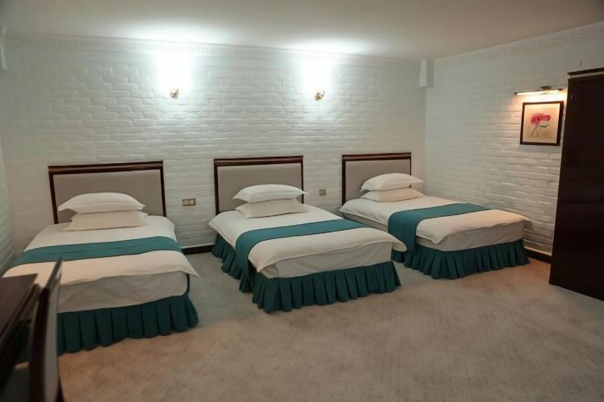 Een kamer met drie bedden, witte bakstenen muren en een ingelijst schilderij aan de muur.