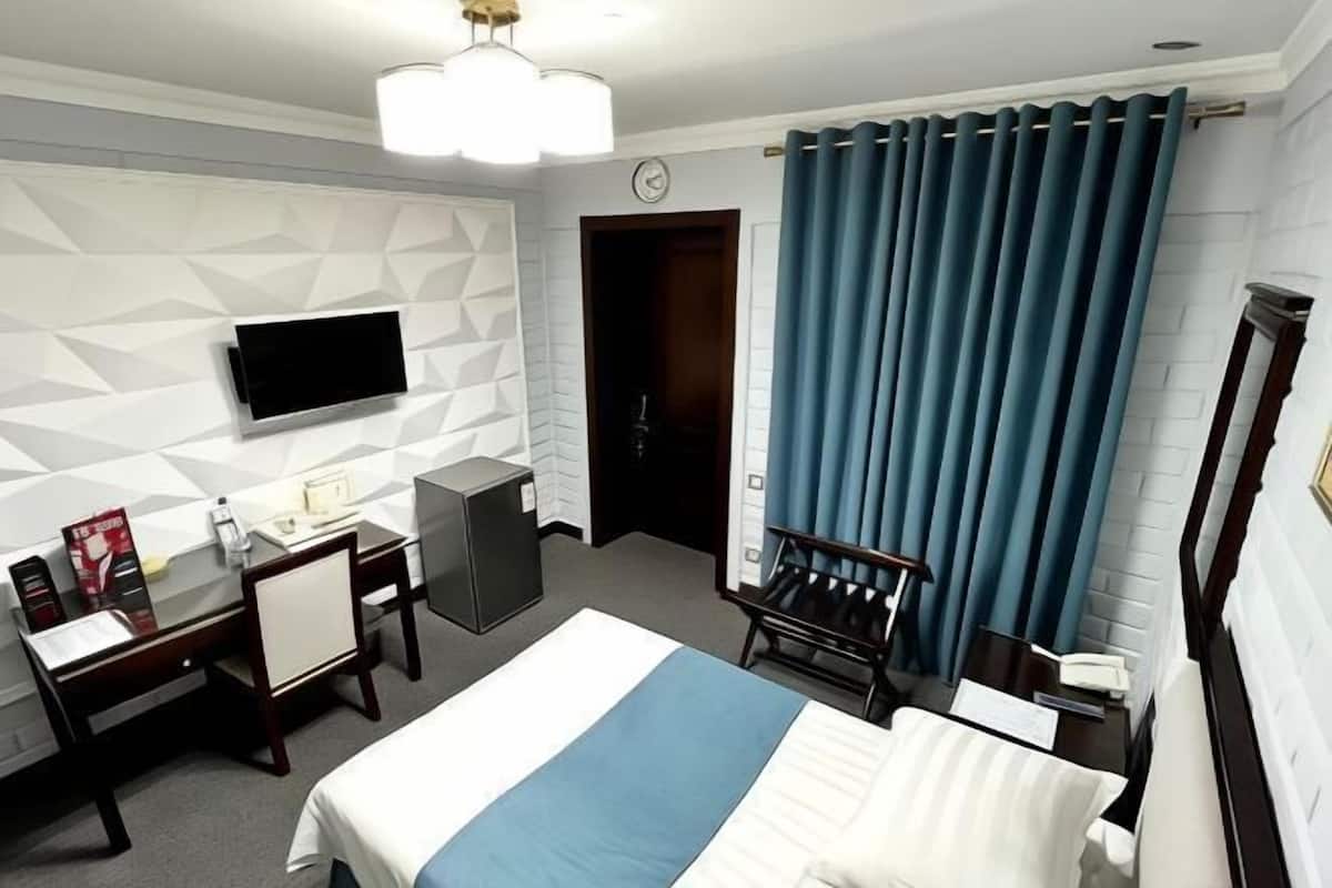Een hotelkamer met een bed, bureau, stoel, televisie en een deur.
