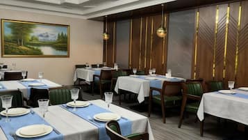 A dining area with tables set for service, a painting on the wall, and a view of a lake.