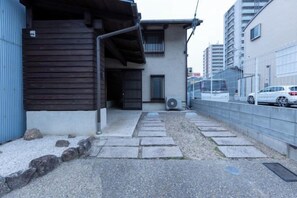 A narrow alleyway with a building on one side and a fence on the other. There are steps leading up to the building, and a car is parked on the right. - MOKUSEKI - Nagoya Japanese Vacation House (Nagoya)