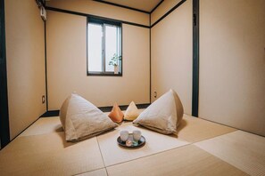 Une pièce avec un sol recouvert de tatamis, une fenêtre, des coussins et un plateau contenant des tasses et une théière.