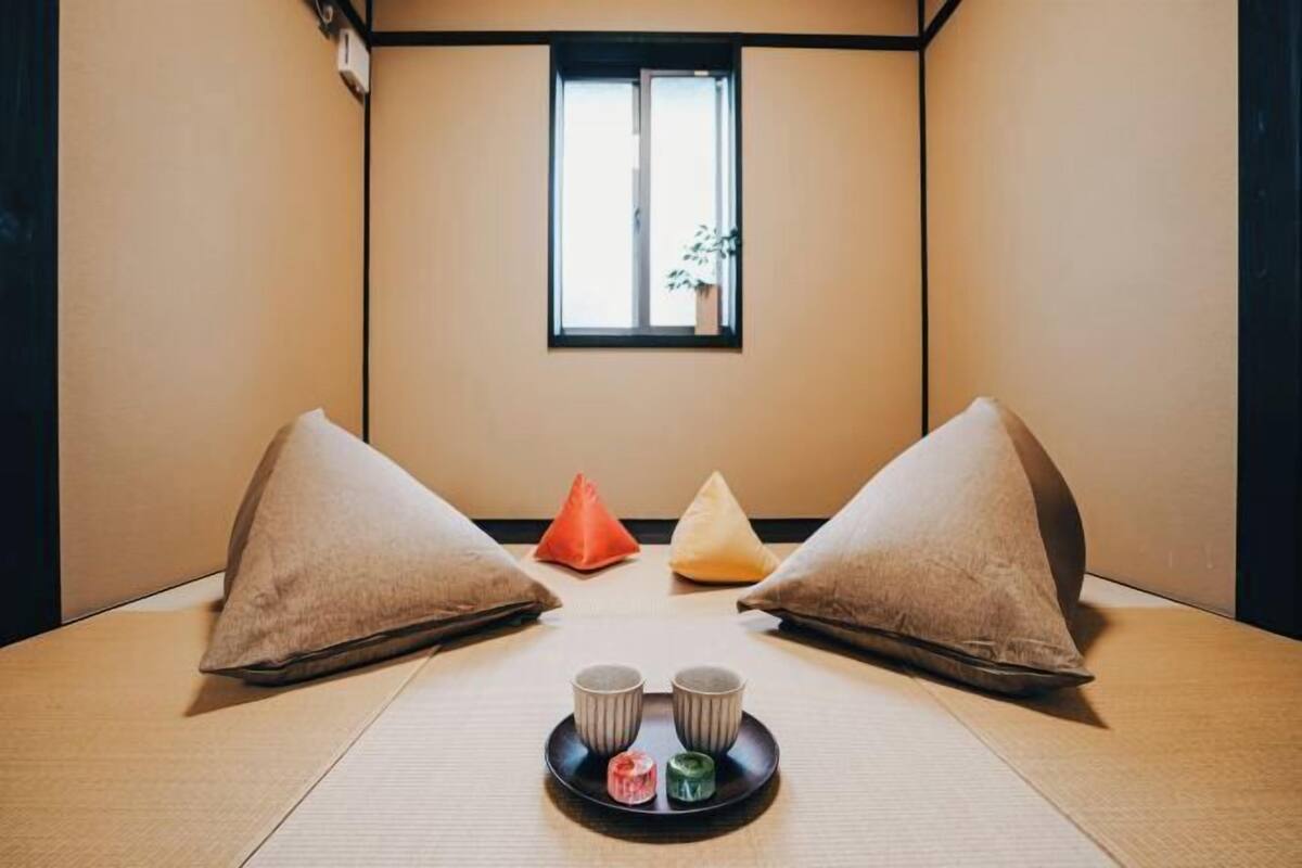 A tatami room with a low table, two pillows, a window, and a tray with two cups and two small containers.