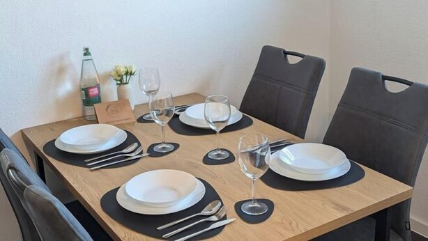A dining table set with plates, cutlery, and glasses, surrounded by chairs. - Q Apartment No. 1 in BS Life close to the city (Braunschweig)
