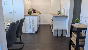 A compact kitchen with white cabinets, a wooden countertop, and a small sink. There are two trash bins and a potted plant on the counter. - Q Apartment No. 1 in BS Life close to the city (Braunschweig)