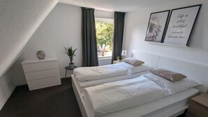 A bedroom with two beds, a bedside table, a nightstand, a window with curtains, and two framed pictures on the wall. - Q Apartment No. 1 in BS Life close to the city (Braunschweig)