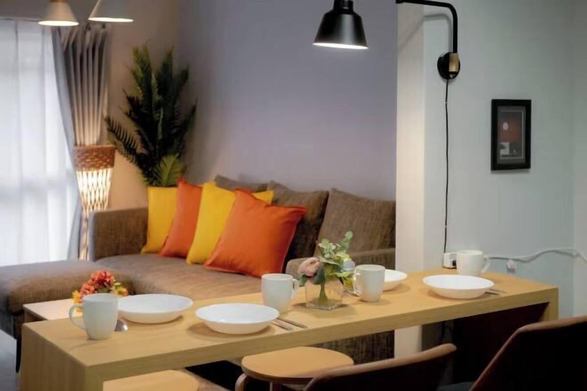 A modern living room with a sofa, a dining table with white plates and cups, and a potted plant.
