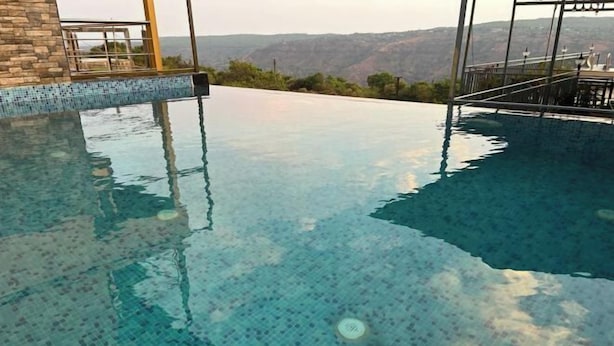 A clear view of a swimming pool with a tiled edge and a view of the surrounding landscape. - Savitri Bungalow (Dhangarwadi)