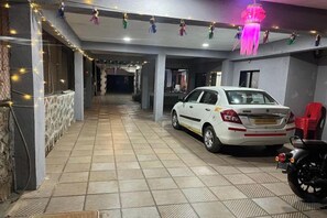 A covered parking area with a white car and a motorcycle, a tiled floor, and a hanging decorative element. - Savitri Bungalow (Dhangarwadi)