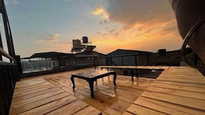 A wooden deck with tables and chairs, overlooking a cityscape during sunset. - Savitri Bungalow (Dhangarwadi)