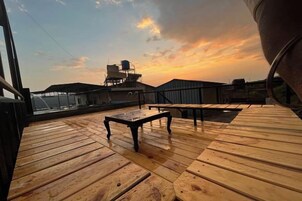 Una terraza de madera con mesas y sillas, con vistas a un paisaje urbano al atardecer.