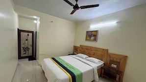 A bedroom with a bed, wooden headboard, bedside tables, a ceiling fan, and a painting on the wall. - Savitri Bungalow (Dhangarwadi)
