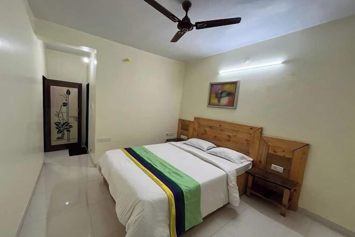 A bedroom with a bed, wooden headboard, bedside tables, a ceiling fan, and a painting on the wall.