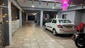 A covered parking area with a white car and a motorcycle, decorated with string lights and hanging ornaments. - Savitri Bungalow (Dhangarwadi)