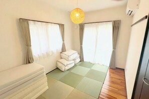 A room with a bed, a sofa, a small table, and a window with curtains. - NewOpen/　NAGO-YA Walking distance to beach Fast WiFi Nature Retreat (Nago)