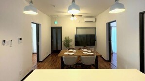 A dining area with a wooden table set for four, two pendant lights, a flat-screen TV, and a potted plant. - NewOpen/　NAGO-YA Walking distance to beach Fast WiFi Nature Retreat (Nago)
