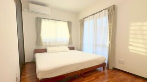 A single bed in a room with wooden flooring, a window with curtains, and an air conditioning unit on the wall. - NewOpen/　NAGO-YA Walking distance to beach Fast WiFi Nature Retreat (Nago)