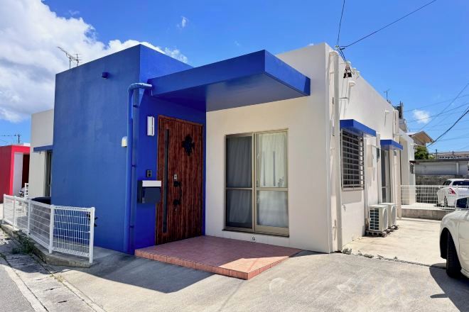 A modern building with a blue and white facade, a wooden door, and a small porch.