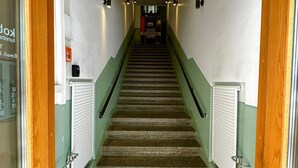Uma escadaria com paredes verdes, corrimão e piso coberto por carpete, levando a uma porta no topo.