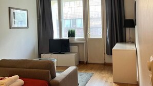 Quarto de hotel moderno com cama, escrivaninha, televisão e janelas amplas.