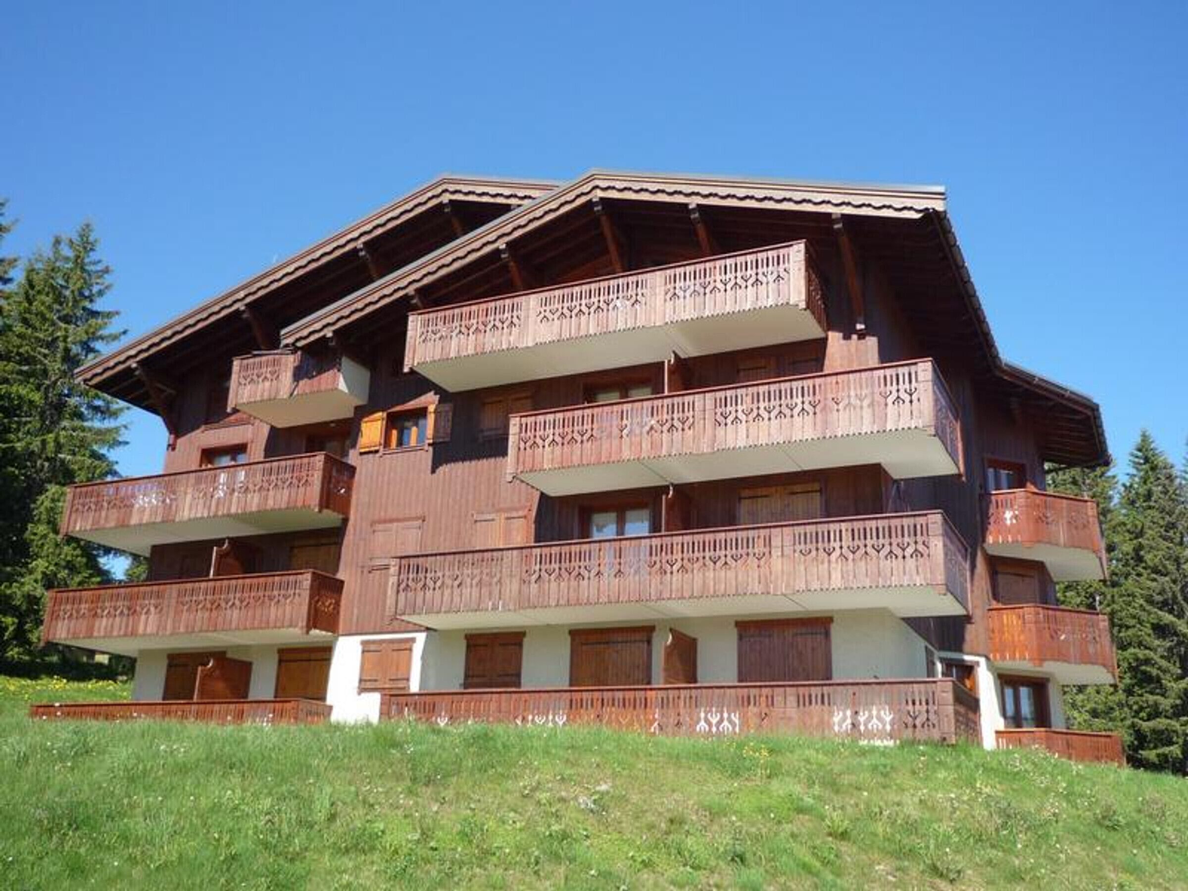 Un edificio de madera de varios pisos con balcones, probablemente un hotel o albergue, ubicado en una zona montañosa con césped verde y árboles.