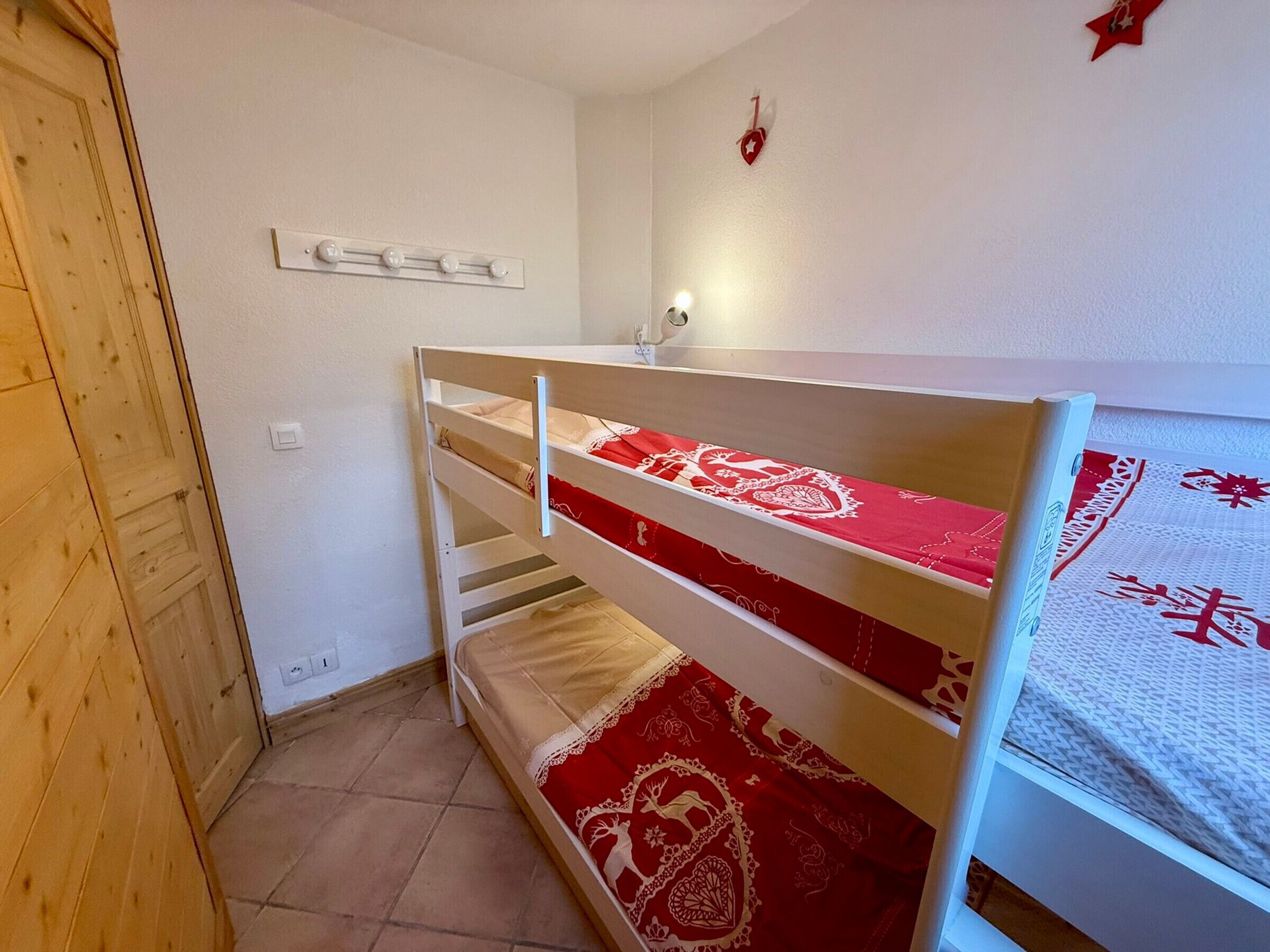 Een stapelbed met rode en witte beddengoed, een houten deur en een wandlamp.