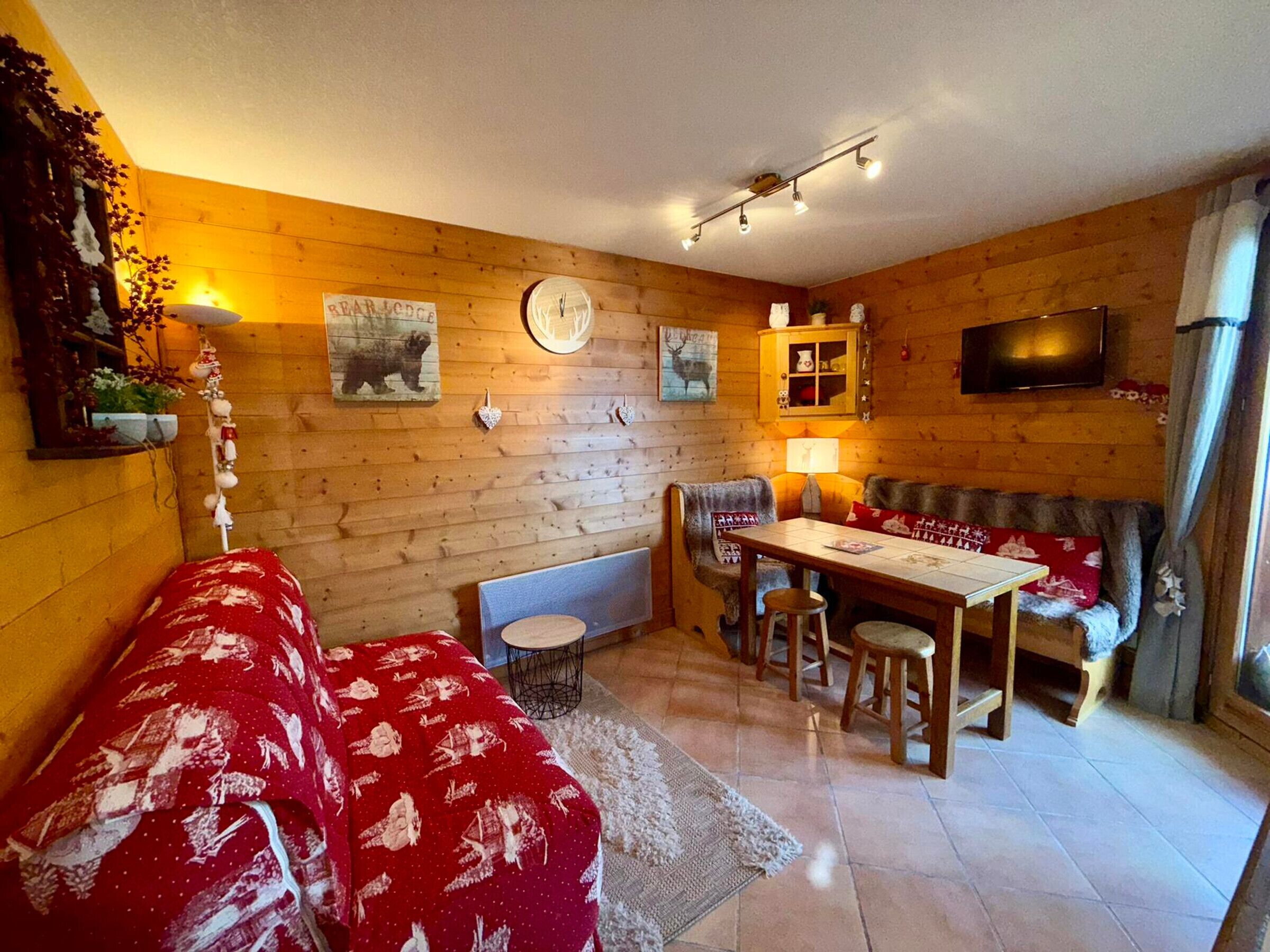 Una habitación estilo cabaña acogedora, con interior de madera, zona de comedor y sofá con funda estampada roja.