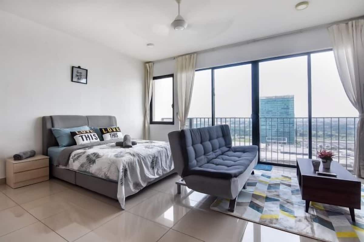A modern bedroom with a bed, a sofa, a nightstand, a desk, and large windows offering a city view.