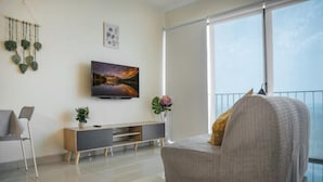 Ein modernes Wohnzimmer mit einer Couch, einem Fernseher, einer Pflanze und einem Balkon mit Geländer.