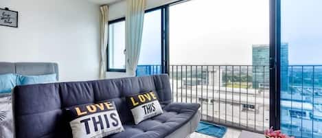 A balcony with a sofa, pillows, a coffee table, and a view of the city.