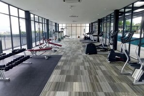 A gym with cardio equipment, weight machines, and a large windowed wall providing natural light. - Lovely Studio Trefoil Near Setia City Mall & SCCC (Shah Alam)