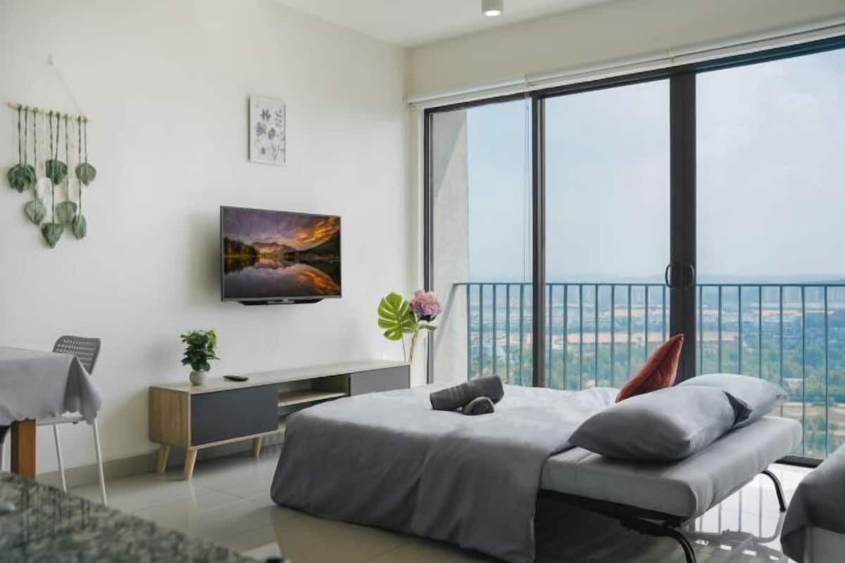 A modern bedroom with a large window, a flat-screen TV, and a balcony with a city view.