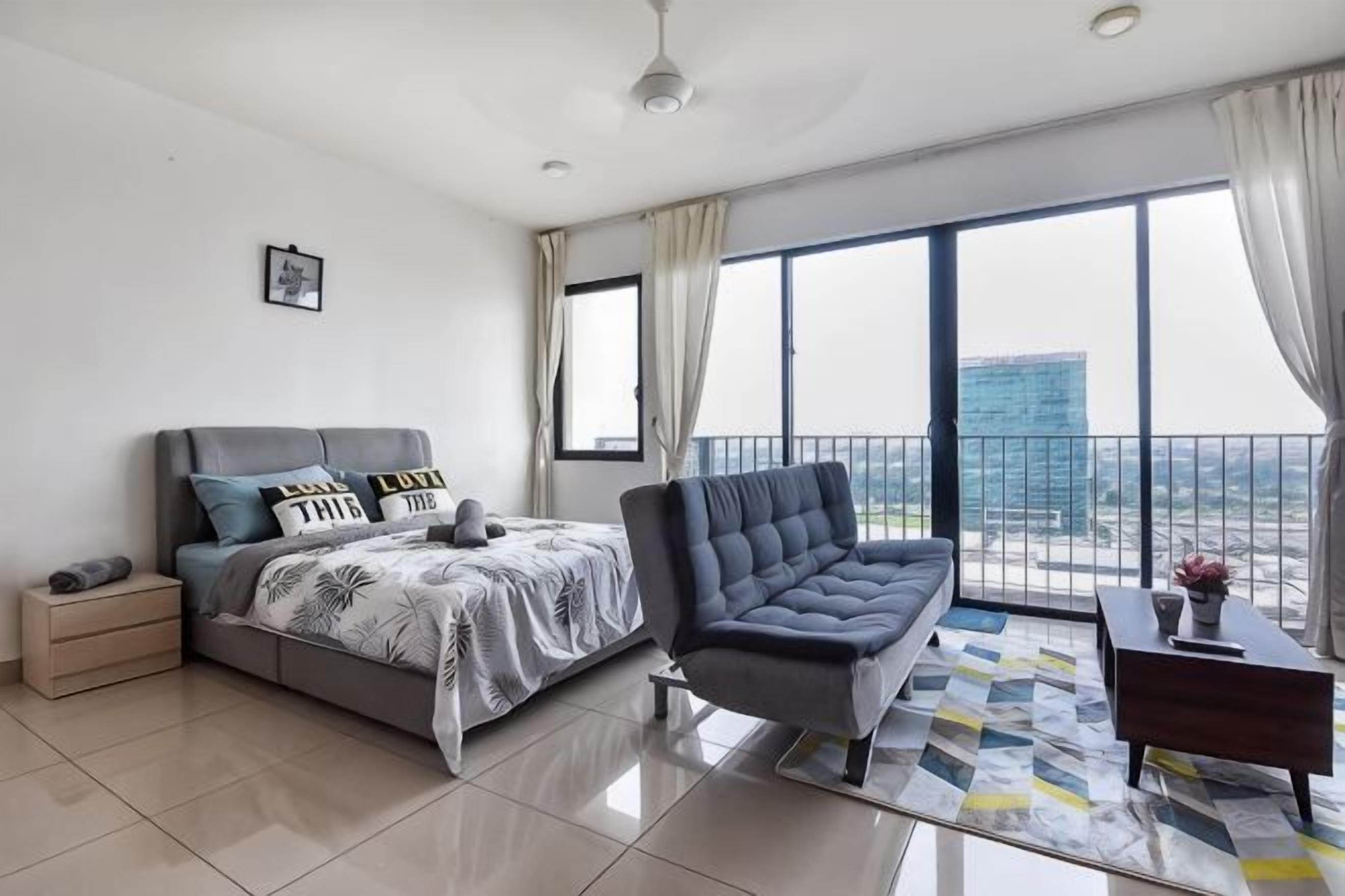 A modern bedroom with a bed, a sofa, a nightstand, and a view of the city.