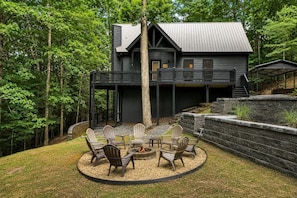 A two-story cabin with a deck, surrounded by a wooded area.
