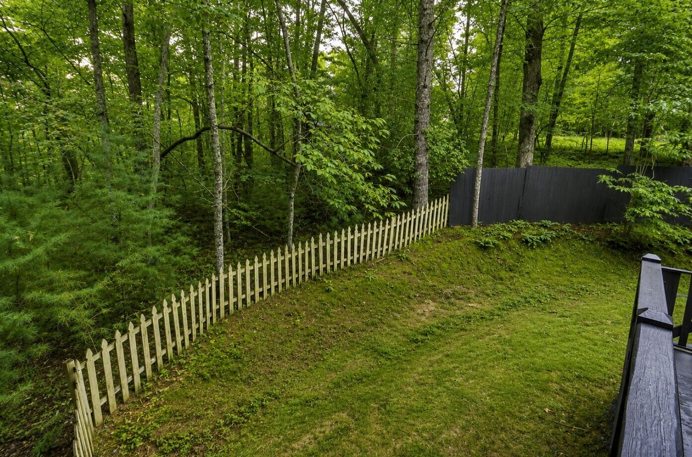 Une cour clôturée, avec une clôture en bois, entourée d’arbres et d’herbe.