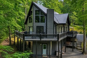 A two-story house with a balcony and a deck, surrounded by trees.