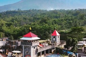 Una estructura que recuerda a un castillo, con una torre del reloj, rodeada de vegetación exuberante y un paisaje montañoso.