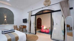 Habitación de hotel con cama, televisión, escritorio, espejo y puerta corrediza de vidrio que da a un balcón.