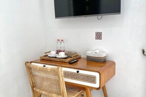 Un escritorio de madera con una silla de mimbre, un televisor en la pared y una bandeja con botellas y vasos.